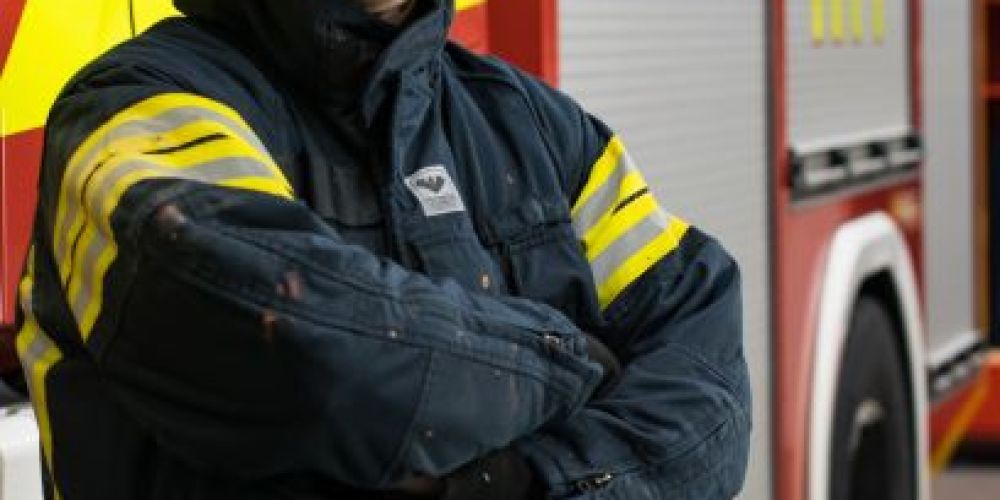Henkilökuva Aleksi Peurala paloasussa kypärä päässä, taustalla paloauto