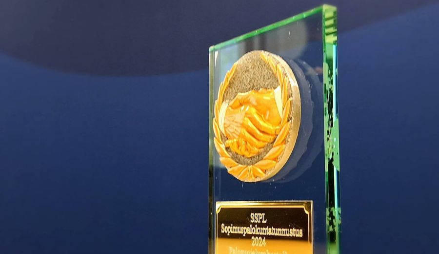 Lasinen sopimuspalokuntatunnuksen muistoesine, taustalla Sisäministeriön sininen kuvaseinä