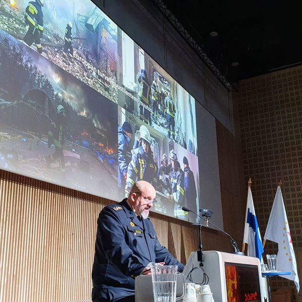 Pelastusylijohtaja Kimmo Kohvakka puhujanpöydän takana Suomen Sopimuspalokuntien Liiton Ajankohtaisseminaarissa Tampere-talolla. Taustalla kuvaesitys kansainvälisestä pelastustoimesta.